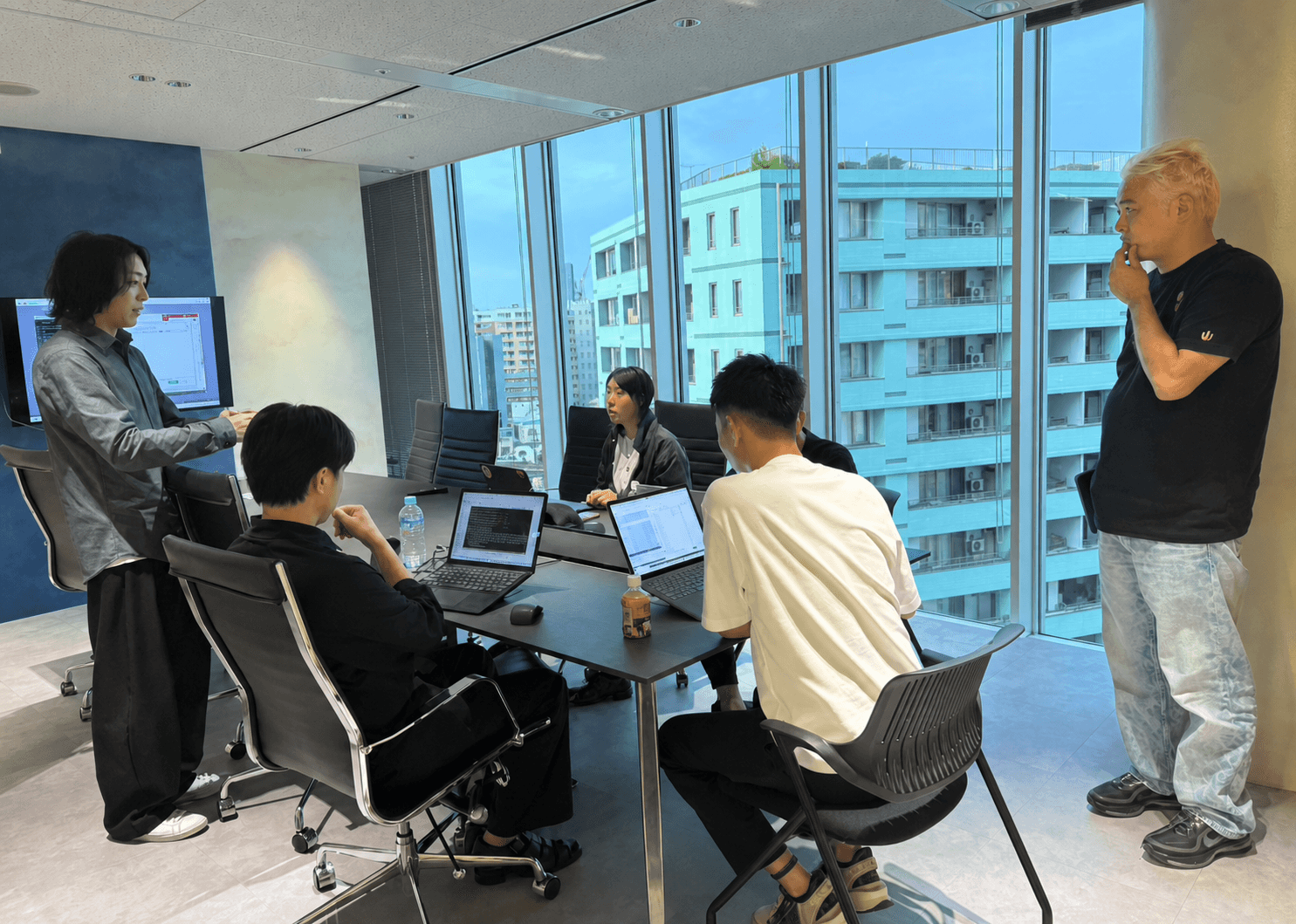 大きな窓の会議室で講師と受講者がAI開発に取り組む研修風景