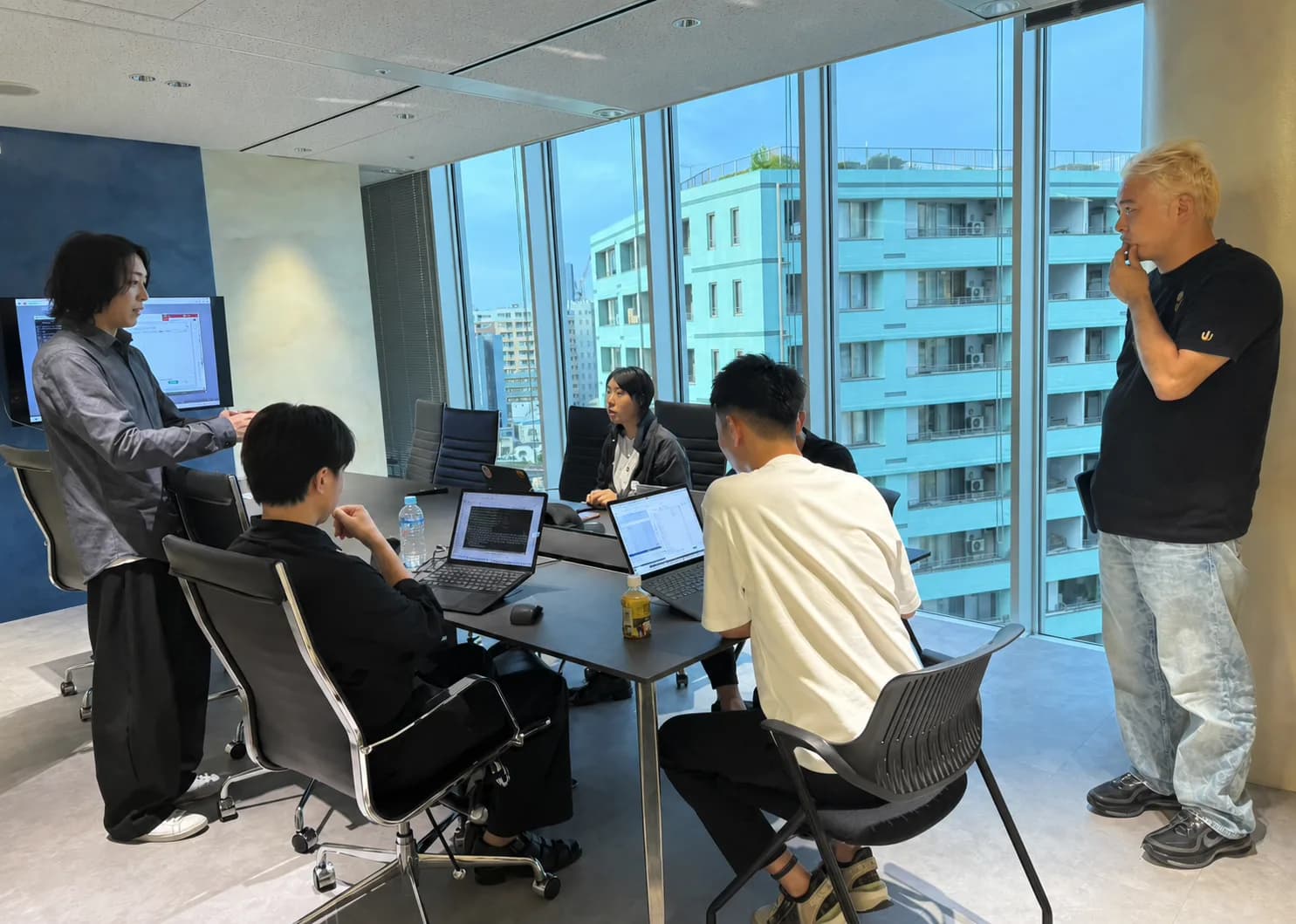 大きな窓の会議室で講師と受講者がAI開発に取り組む研修風景